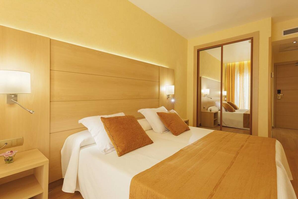 Una habitación de hotel con una cama grande, dos lámparas de noche, una mesita de noche y un espejo.