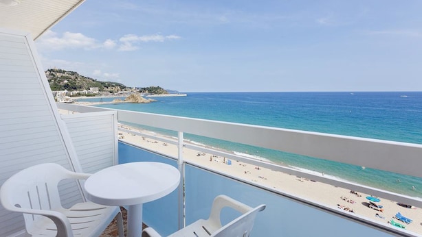 A balcony with a view of a beach, a table, and two chairs. - Hotel Pimar & Spa (Blanes)