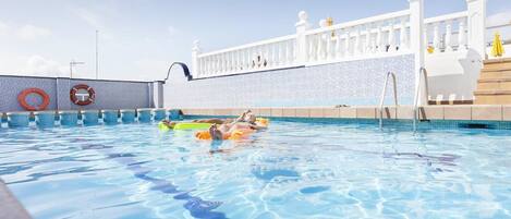 Una piscina con agua azul cristalina, una cerca blanca y un muro de azulejos.