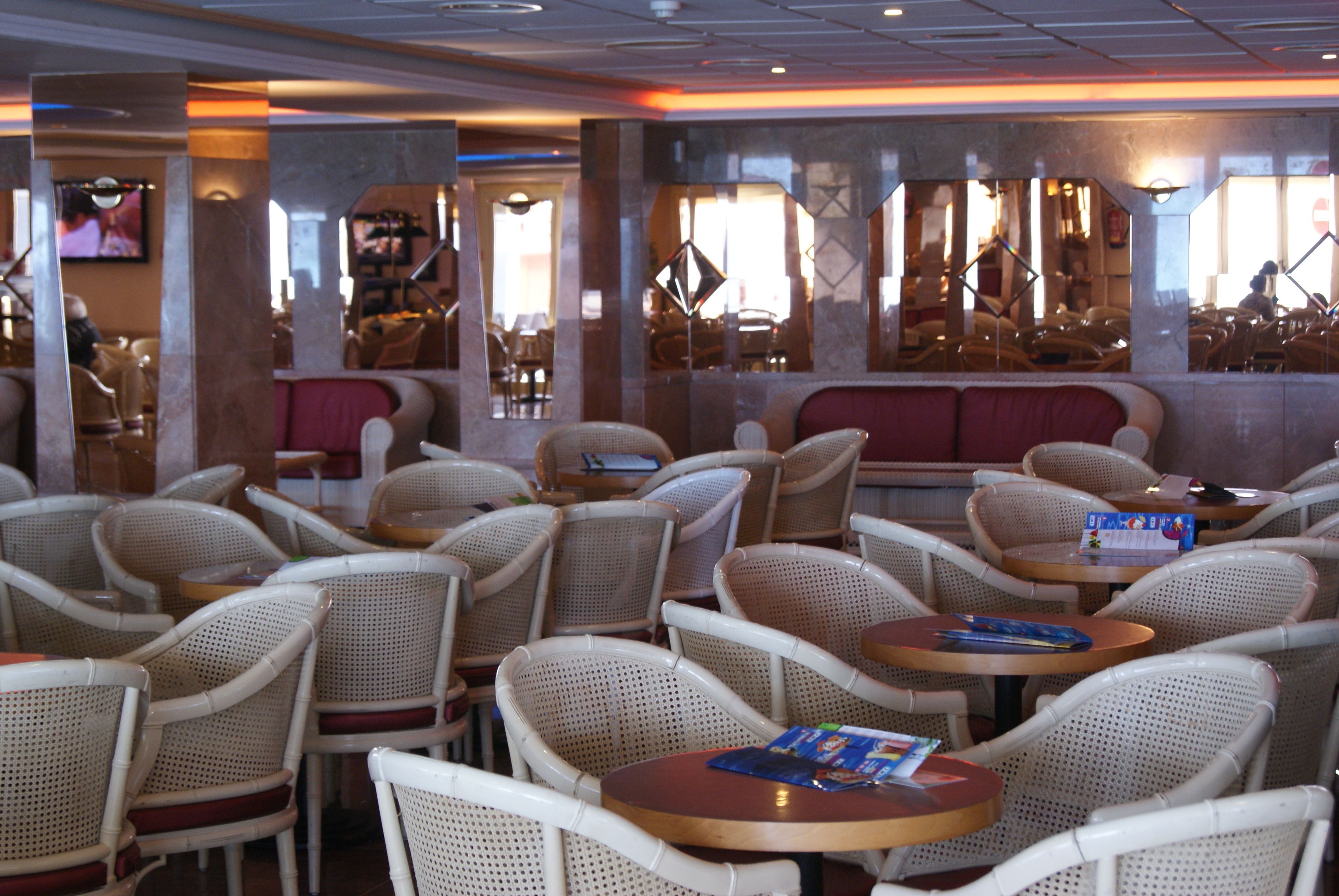 A restaurant with wicker chairs and round tables, a red cushioned bench, and a television mounted on the wall.