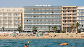 A hotel with multiple balconies, a beach in the foreground, and people kayaking. - Hotel Pimar & Spa (Blanes)