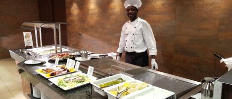A buffet setup with various food items and a chef in uniform.