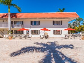 A two-story building with a red-tiled roof, outdoor seating area with red umbrellas, and a paved patio. - Hibiscus Suites - Gateway to Siesta Key (Sarasota)