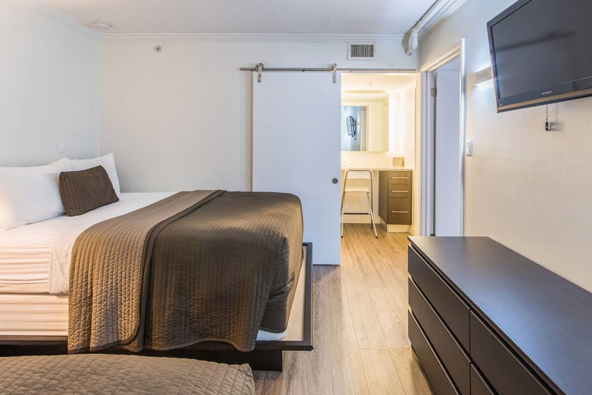 A bedroom with a bed, a dresser, and a TV mounted on the wall.