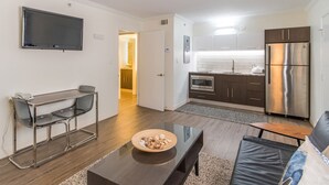 Een modern appartement met woonkamer, een eethoek, een keuken en een aan de muur bevestigde televisie.
