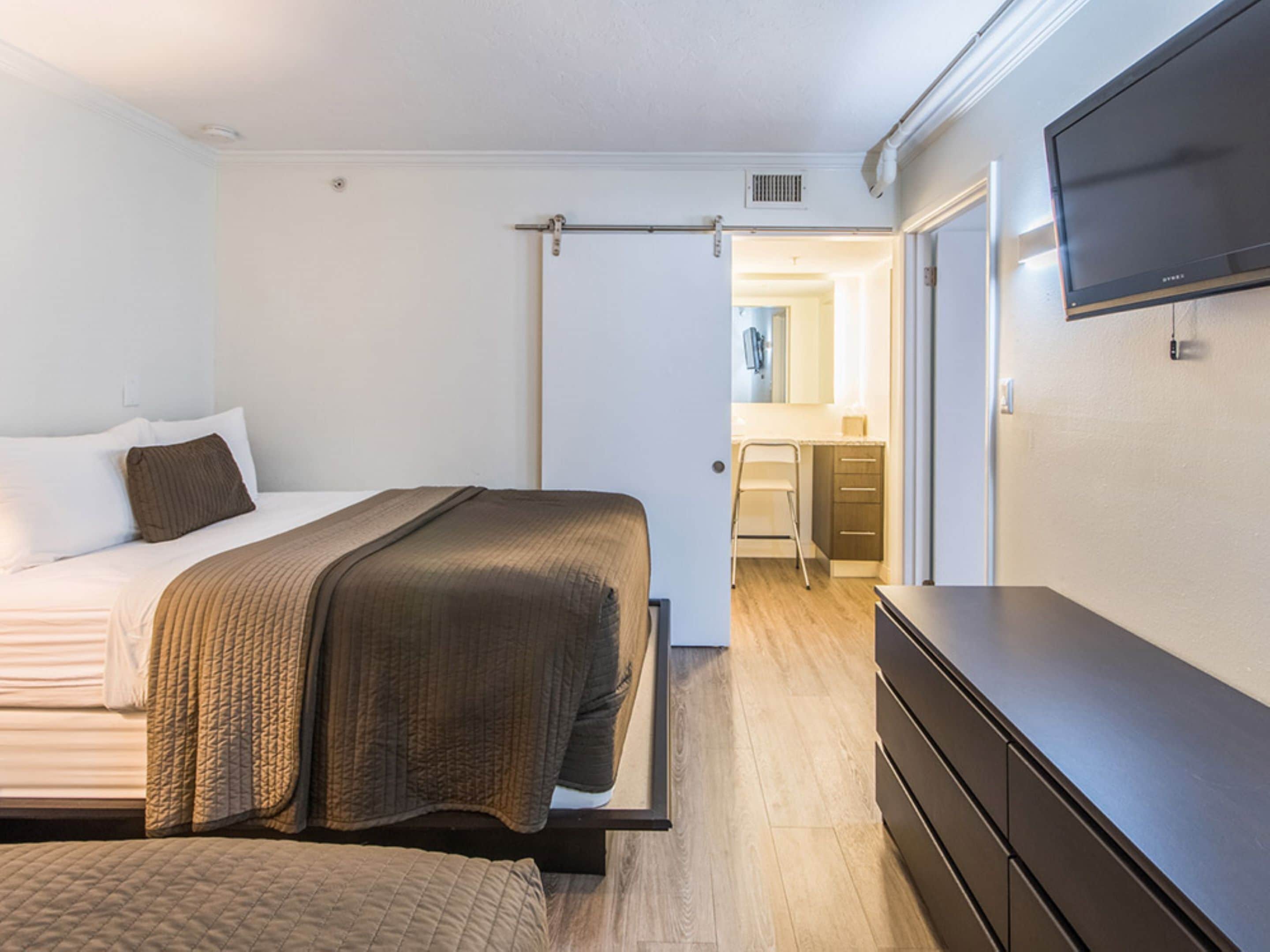 Un dormitorio con cama, cómoda y televisor en la pared.
