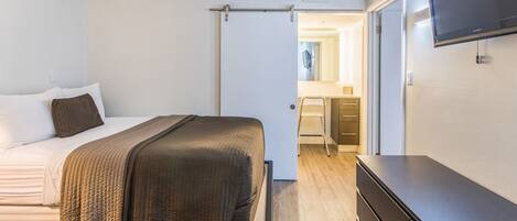 A bedroom with a bed, a dresser, and a television on the wall.