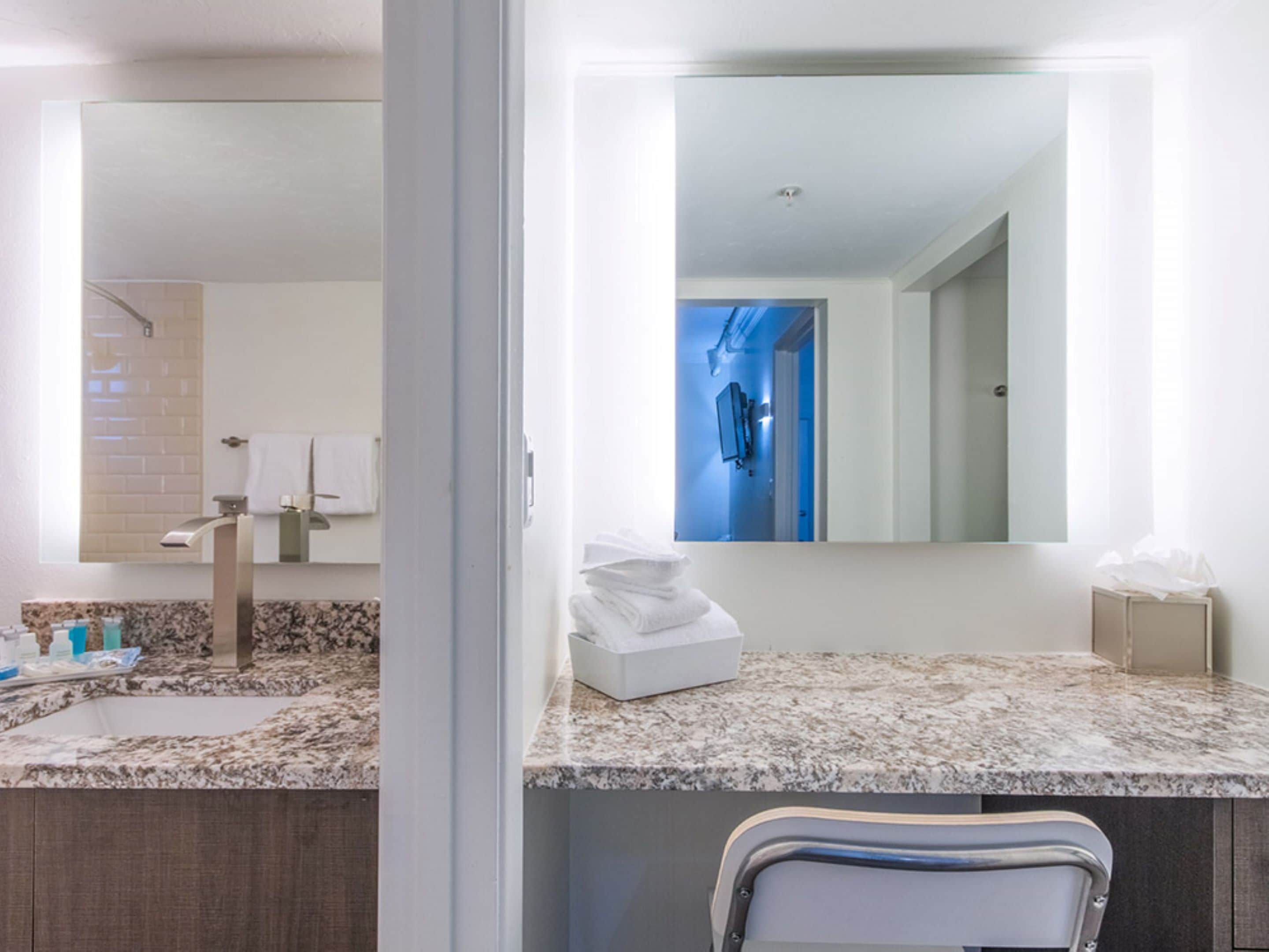 A modern bathroom with a granite countertop, a sink, a mirror, and a towel rack.
