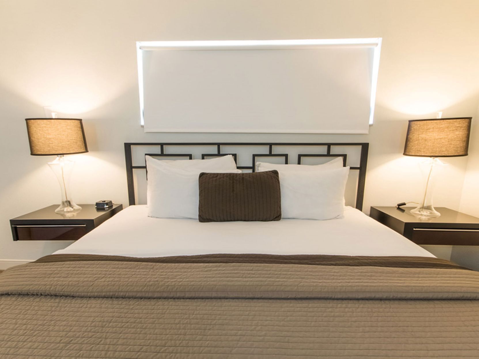 A neatly made bed with a headboard, two bedside tables with lamps, and a window above the bed.