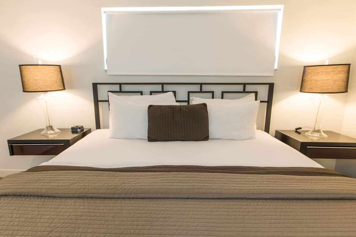 A neatly made bed with a headboard, two bedside tables with lamps, and a window above the bed.