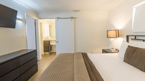 Een hotelkamer met een bed, een aan de muur bevestigde televisie, een nachtkastje met een lamp en een kledingkast.