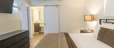 A hotel room with a bed, a TV mounted on the wall, a bedside table with a lamp, and a wardrobe.