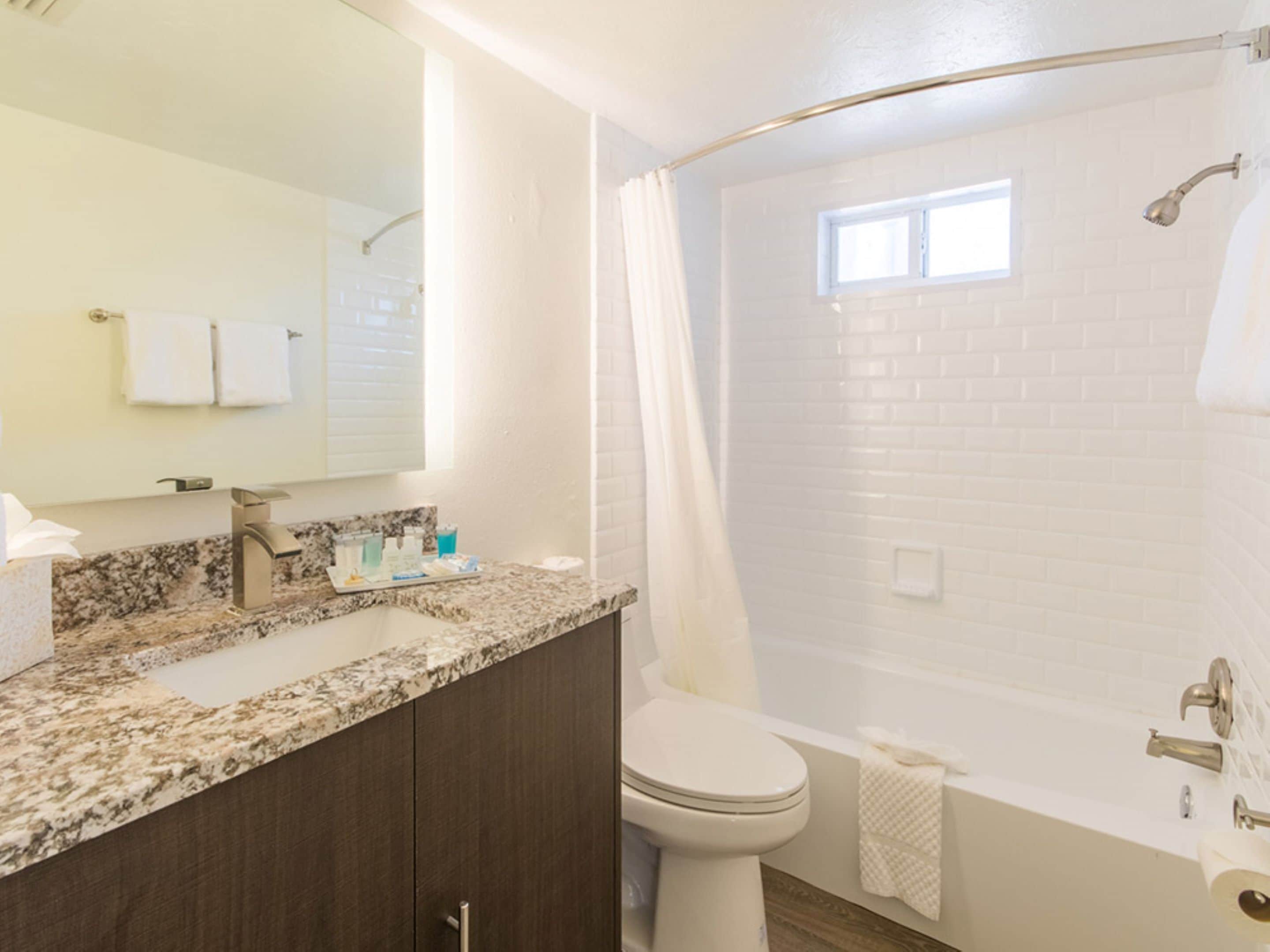 A bathroom with a granite countertop, a white toilet, a bathtub, and a shower curtain.