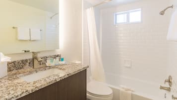 A bathroom with a granite countertop, a white toilet, a bathtub, and a shower curtain.