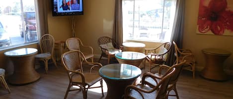 A room with wicker furniture, a TV on the wall, and large windows.
