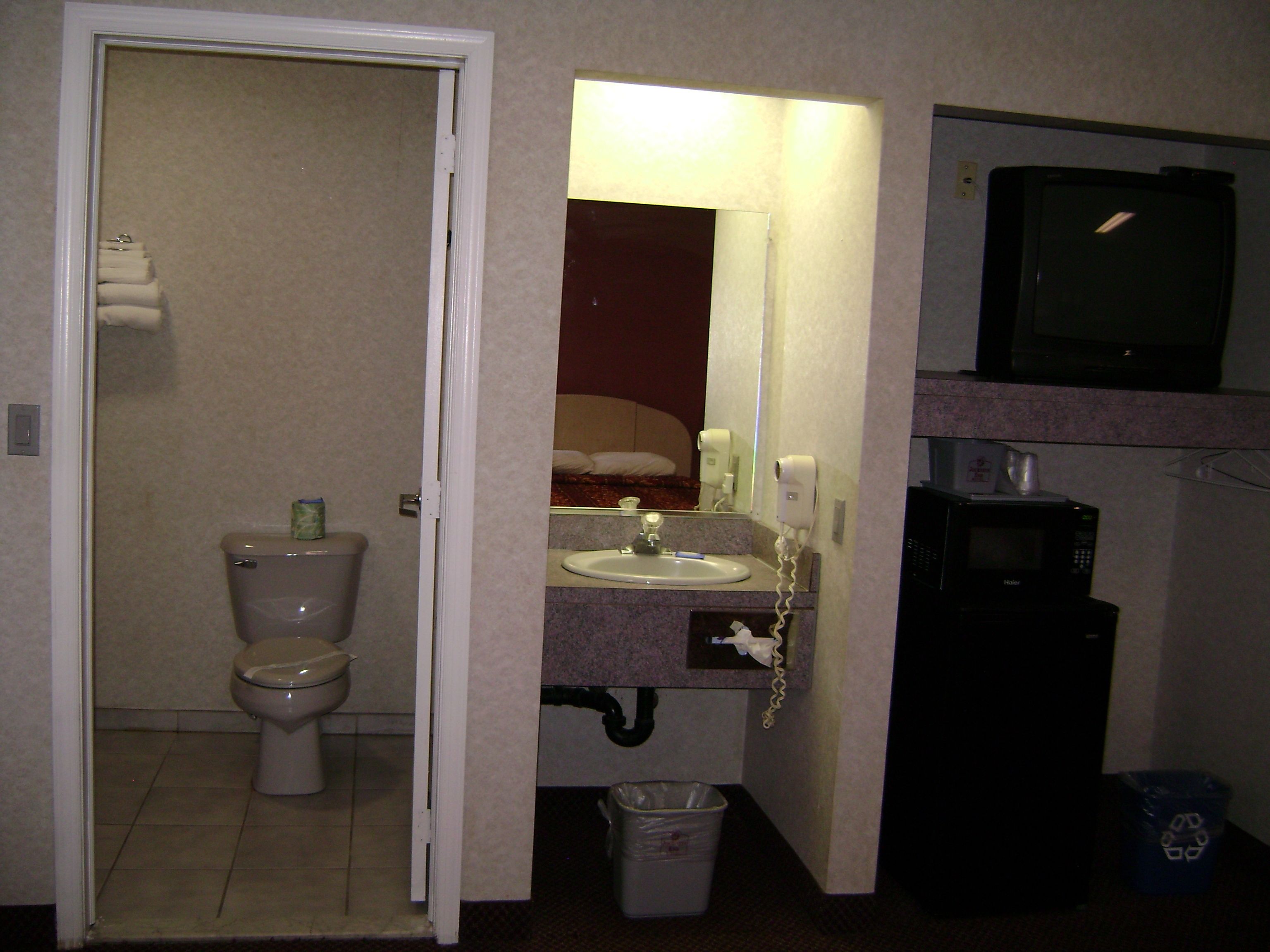 Un baño con inodoro, lavamanos, espejo, secador de pelo y televisión.