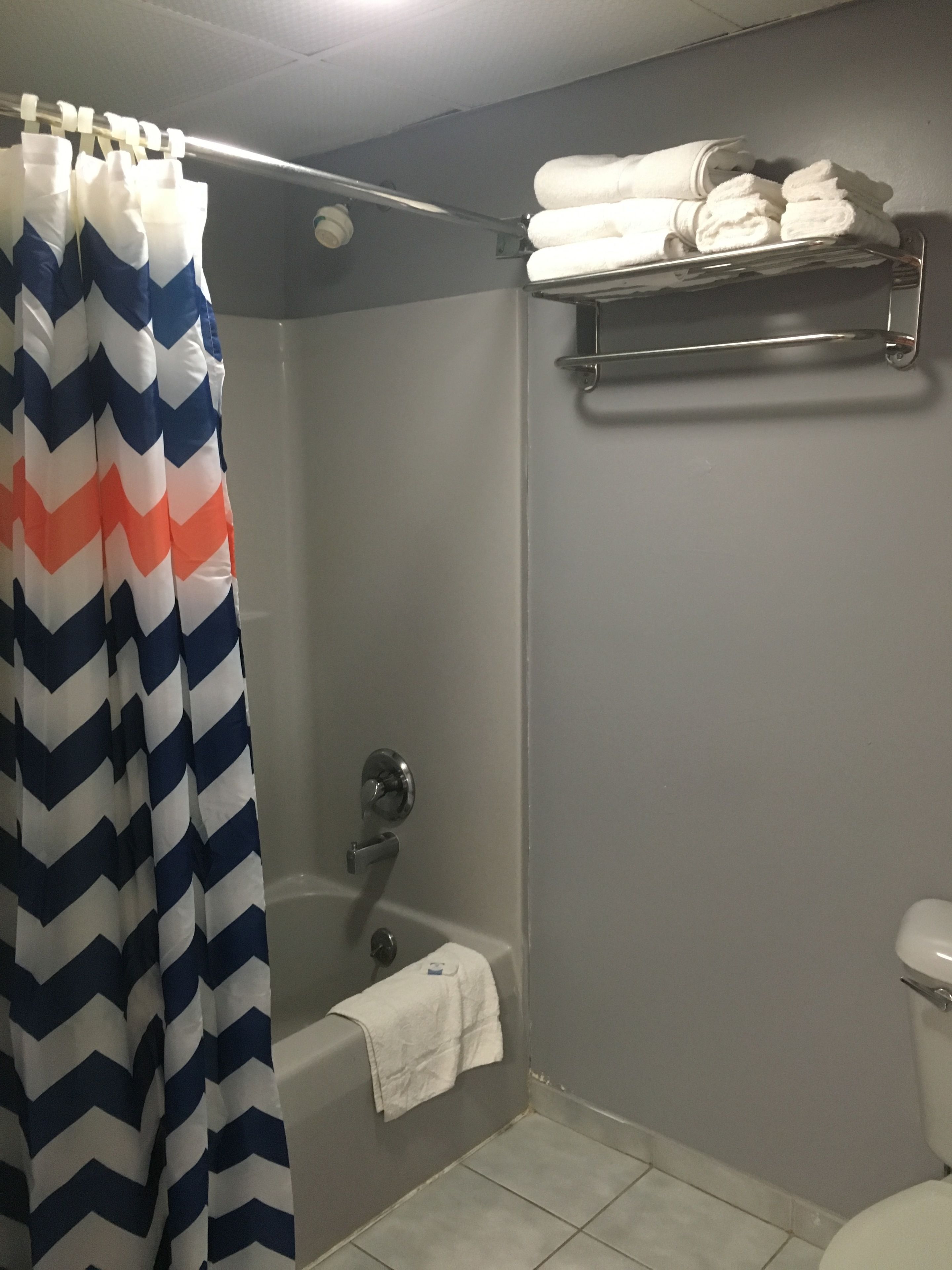 Un baño con cortina de ducha, bañera, inodoro y toallero con toallas dobladas.