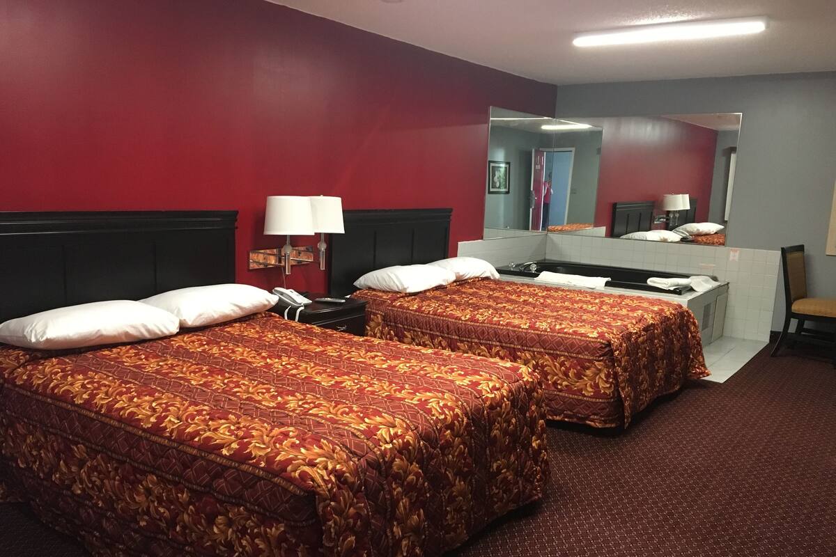 A hotel room with two beds, a desk, a mirror, and a chair.