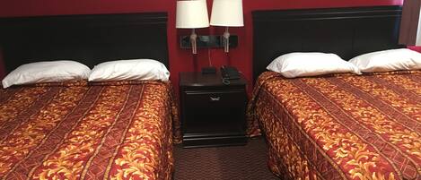 A hotel room with two beds, each with a red and gold patterned bedspread, a black nightstand with a lamp, and a red wall.