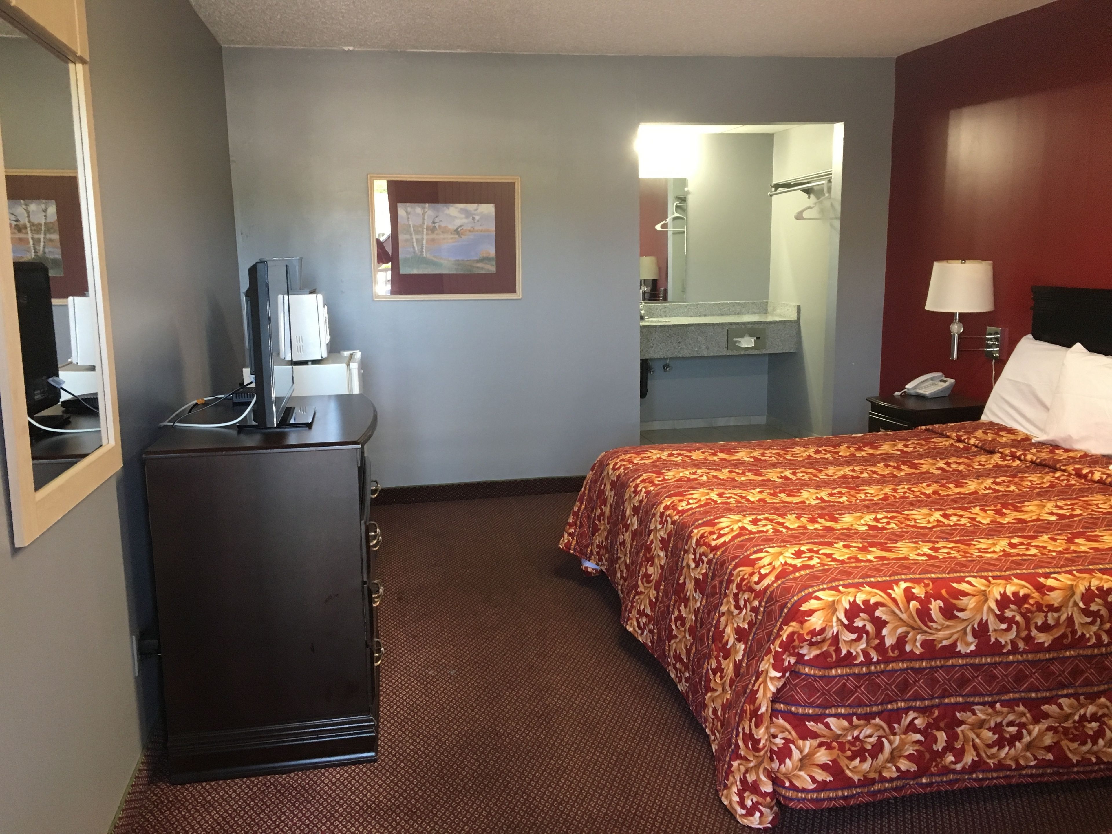A hotel room with a bed, a desk, a dresser, a mirror, and a bathroom visible through an open door.