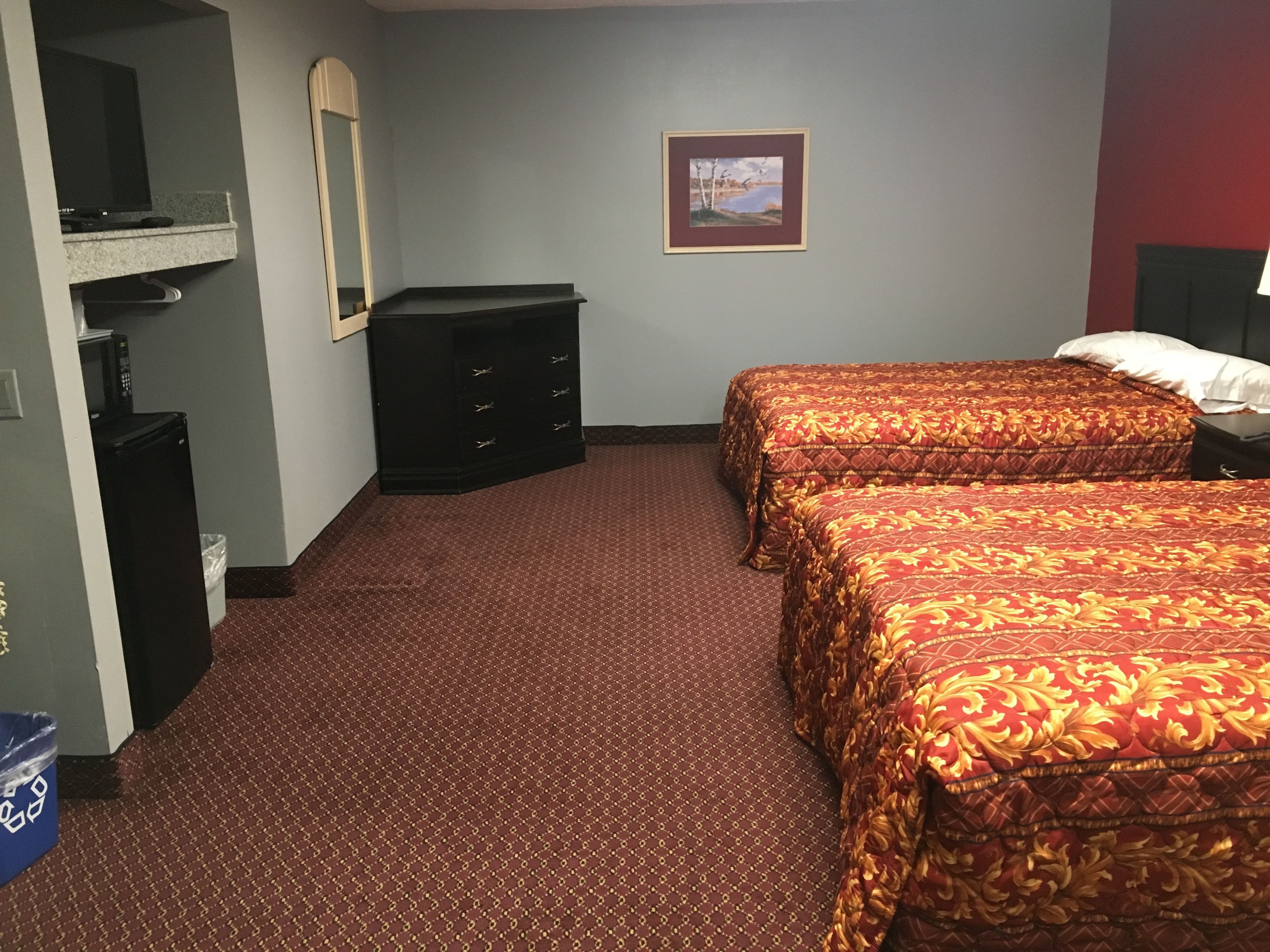 Une chambre d’hôtel avec deux lits, une commode, un téléviseur et un tableau encadré au mur.