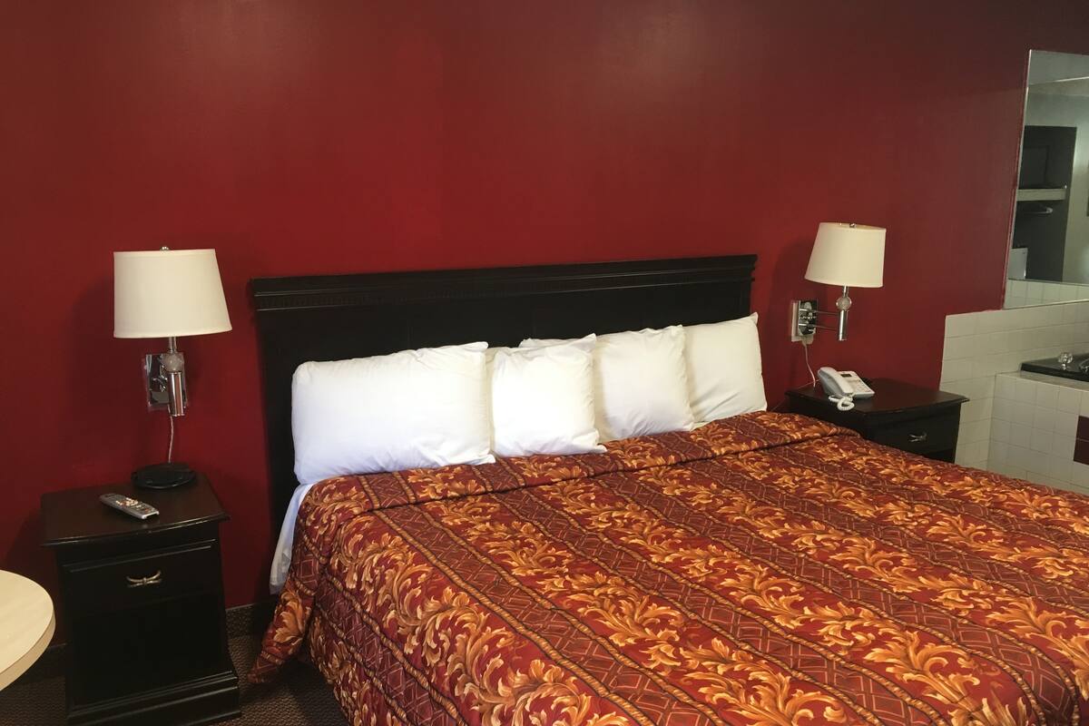 A hotel room with a large bed, two bedside tables with lamps, a telephone, and a mirror on the wall.
