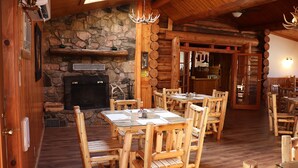 A rustic wooden interior with a stone fireplace, wooden tables and chairs, and a ceiling fan. - Yellowstone Valley Inn (Wapiti)