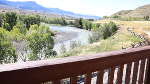 A river with a wooden railing in the foreground, surrounded by greenery and mountains in the background. - Yellowstone Valley Inn (Wapiti)