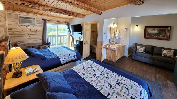 A cabin with two beds, a sofa, a bathroom with a sink and mirror, and a painting on the wall. - Yellowstone Valley Inn (Wapiti)
