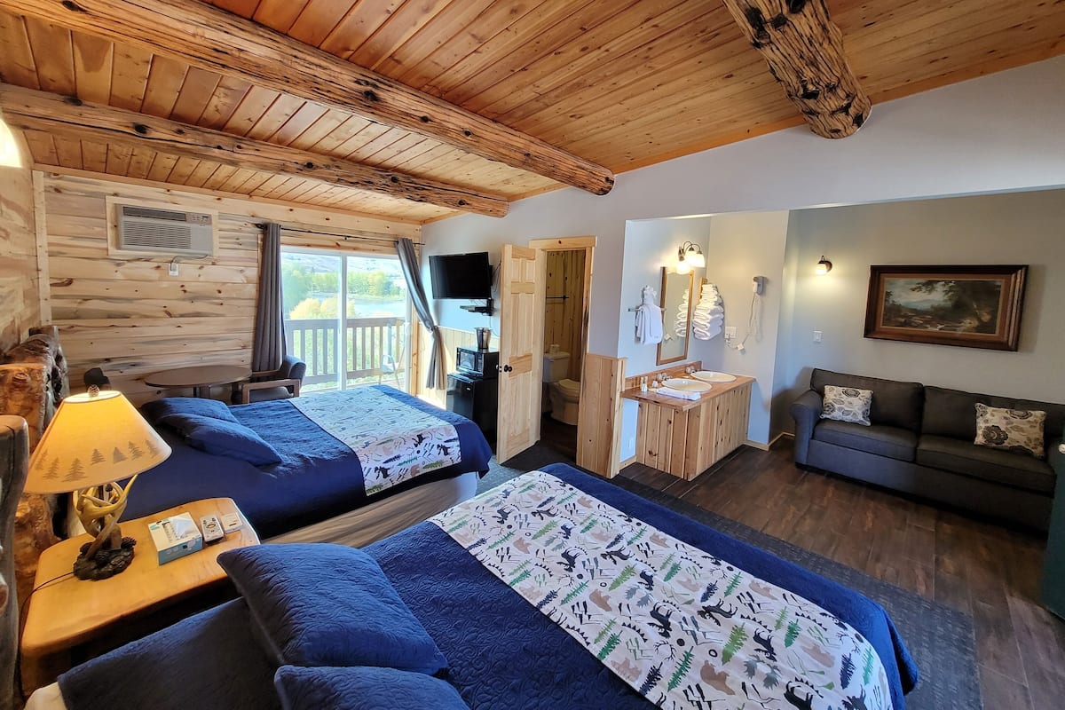 A cabin with two beds, a sofa, a bathroom with a sink and mirror, and a painting on the wall.