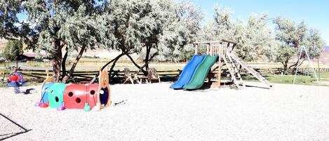 A playground with a slide and swings, surrounded by trees.