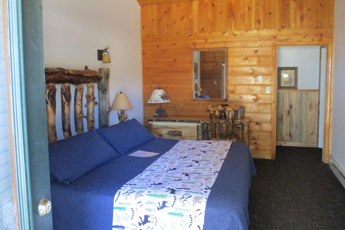 A wooden cabin room with a bed, a desk, a mirror, and a lamp.