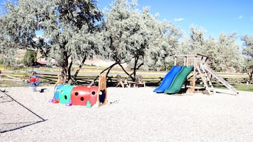 Explore the outdoor playground with a slide and climbing frames set amidst lush trees.