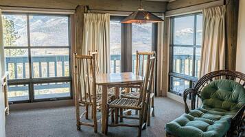 A room with a wooden dining table and chairs, a green upholstered chair, and large windows with curtains.