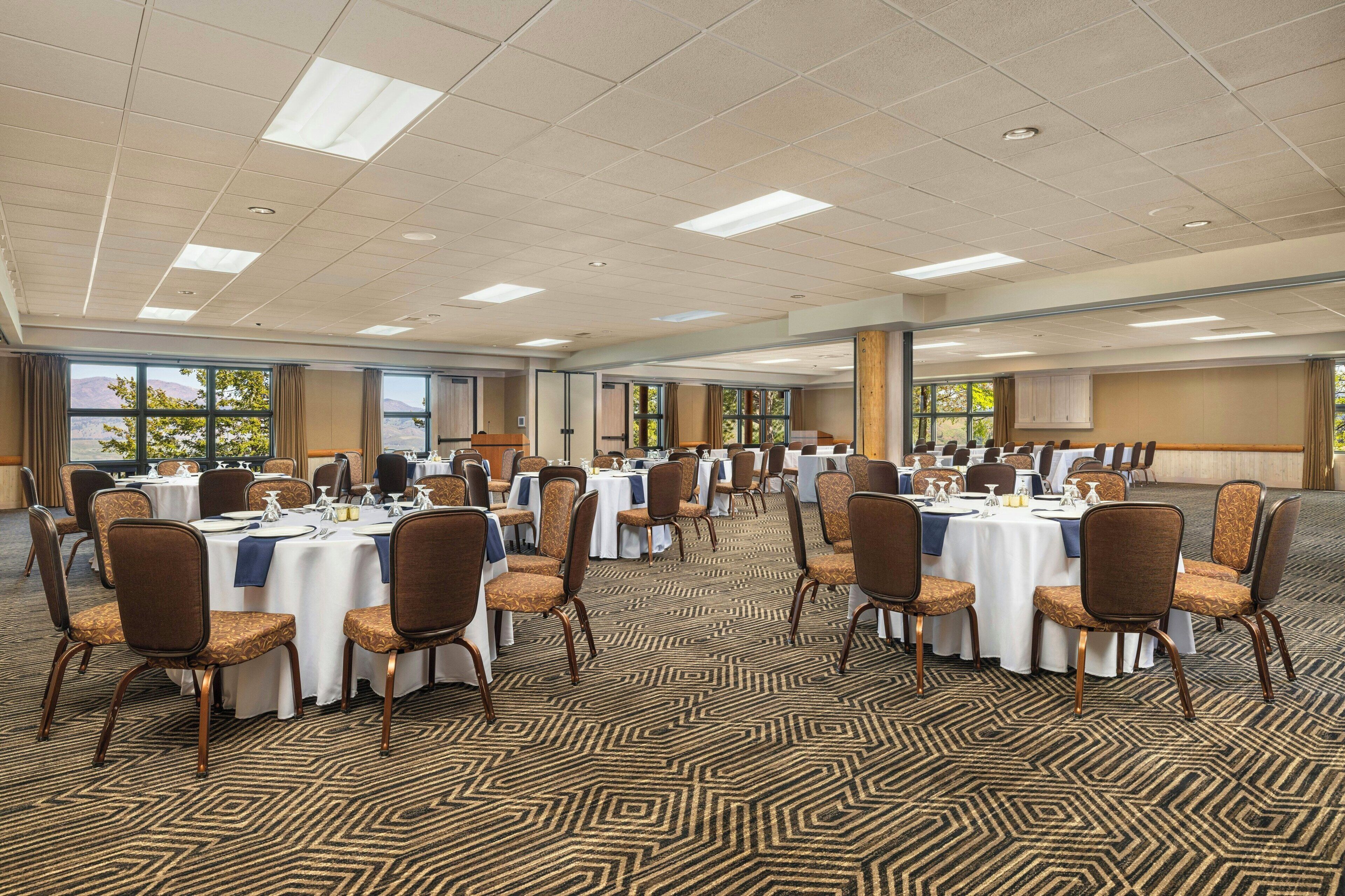 A conference room with multiple tables and chairs, large windows with curtains, and a patterned carpet.