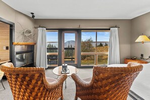 Una habitación con dos sillas de mimbre orientadas hacia una mesa, una chimenea y vistas a un paisaje montañoso a través de amplios ventanales.
