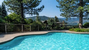 A clear swimming pool with a curved edge, surrounded by a wooden fence and trees. - Sun Mountain Lodge (Winthrop)
