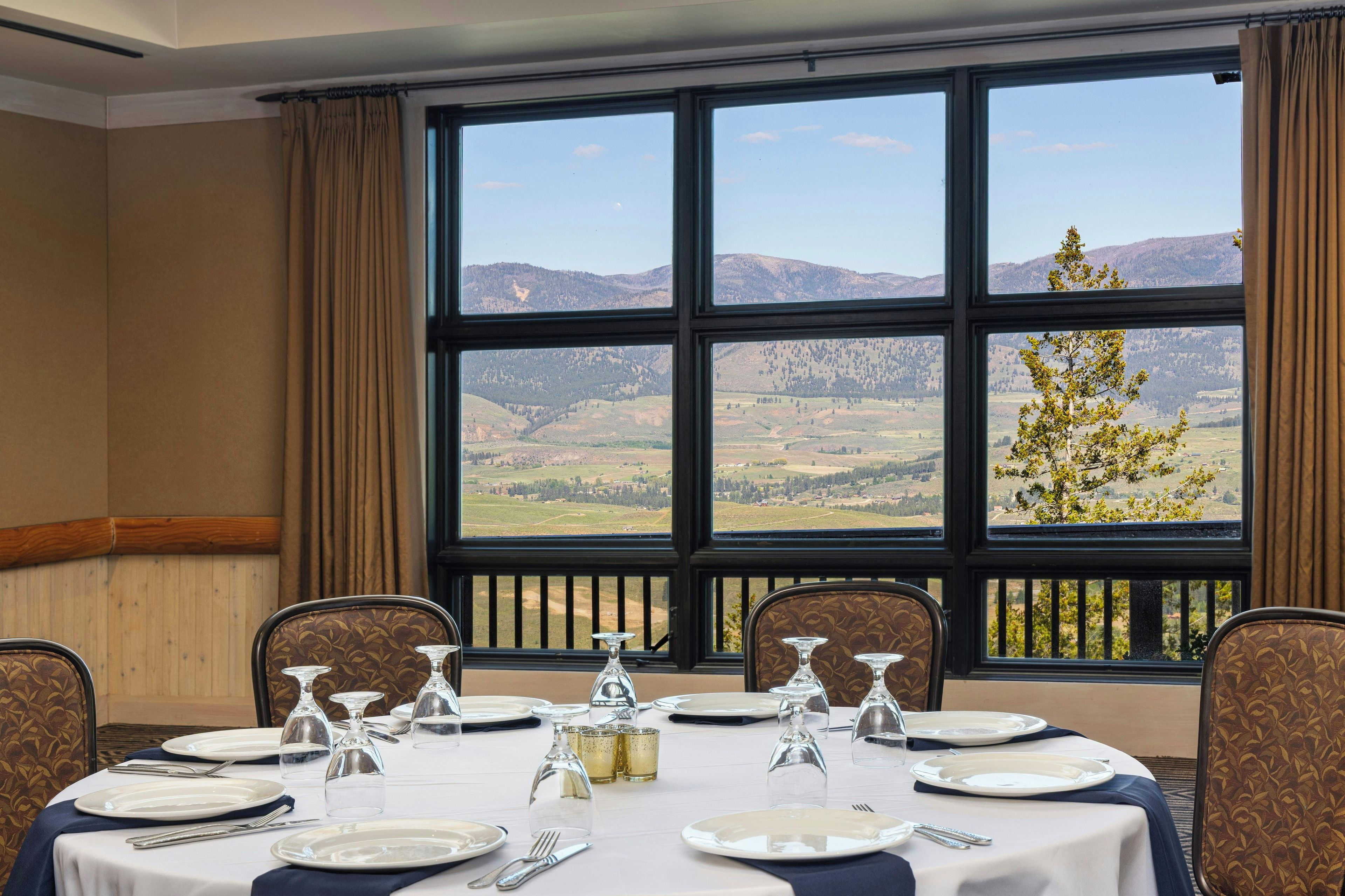 Un comedor con una mesa dispuesta para seis personas, ventanas amplias con vistas a la montaña y al campo.