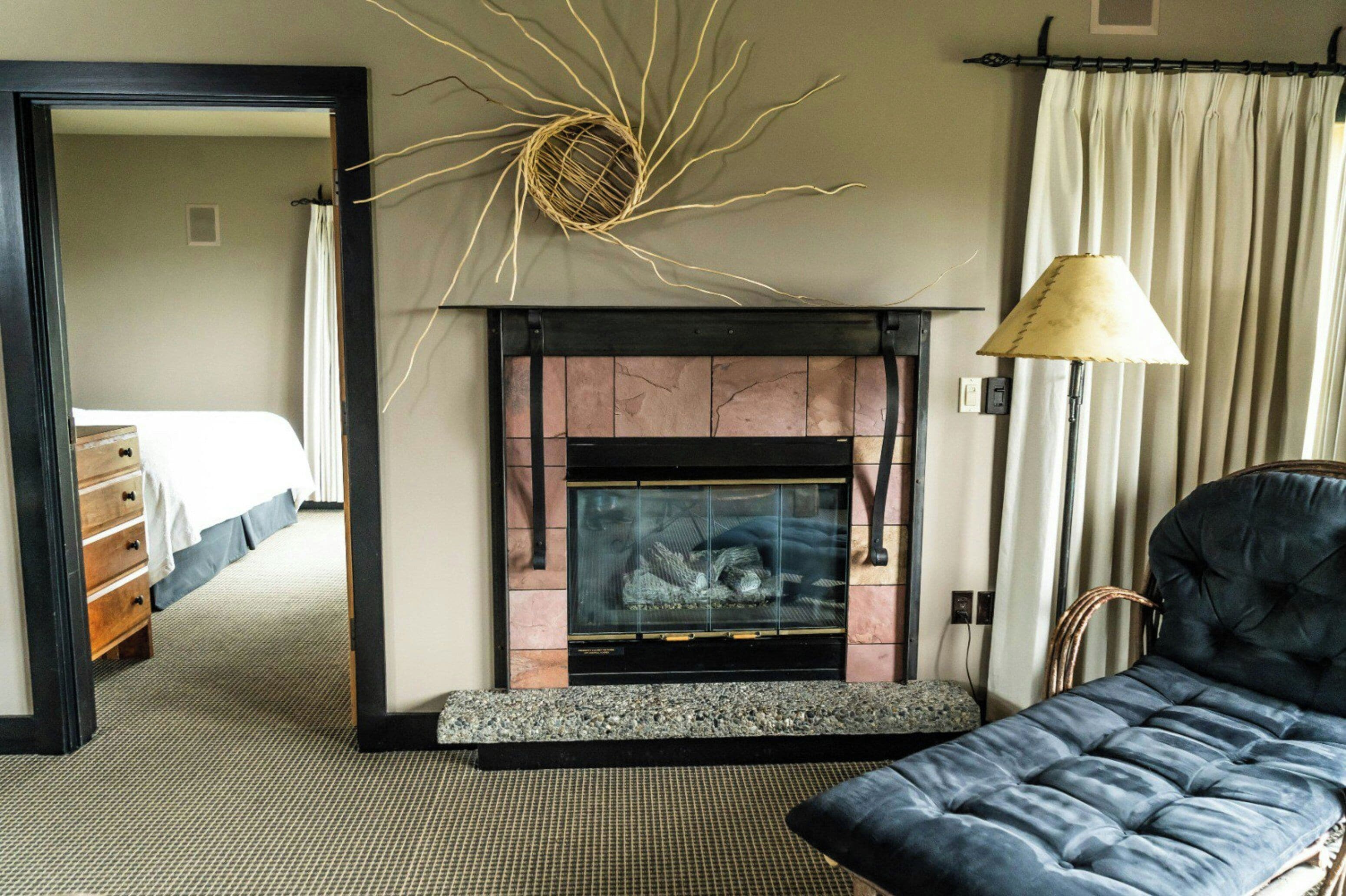 A hotel room with a fireplace, a sofa, a lamp, and a bed.