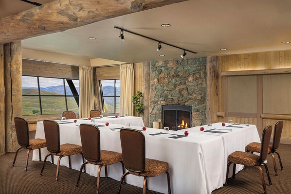 A conference room with a fireplace, large windows, and a view of the mountains.
