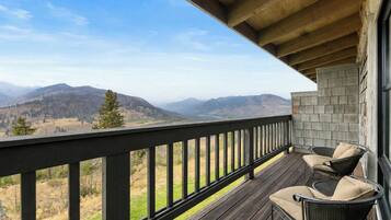 A wooden deck with a view of mountains, a wicker chair, and a stone wall.