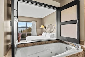A modern hotel room with a large bed, a bathroom with a bathtub, and a view of the outdoors. - Sun Mountain Lodge (Winthrop)