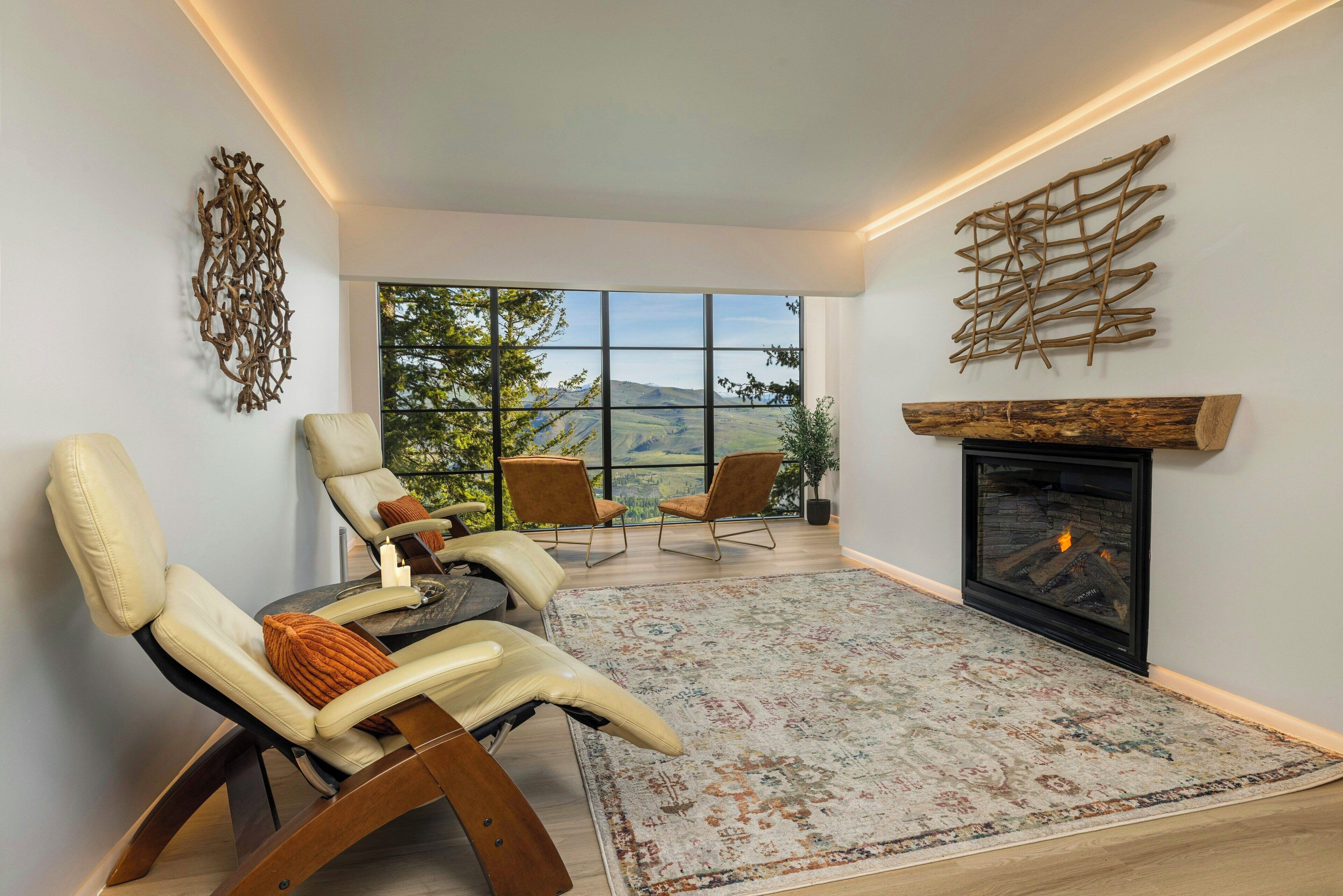 A modern living room with a fireplace, leather chairs, a large window with a view, and decorative wall art.