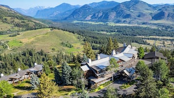 Una cabaña con varias construcciones, rodeada de colinas y montañas boscosas.