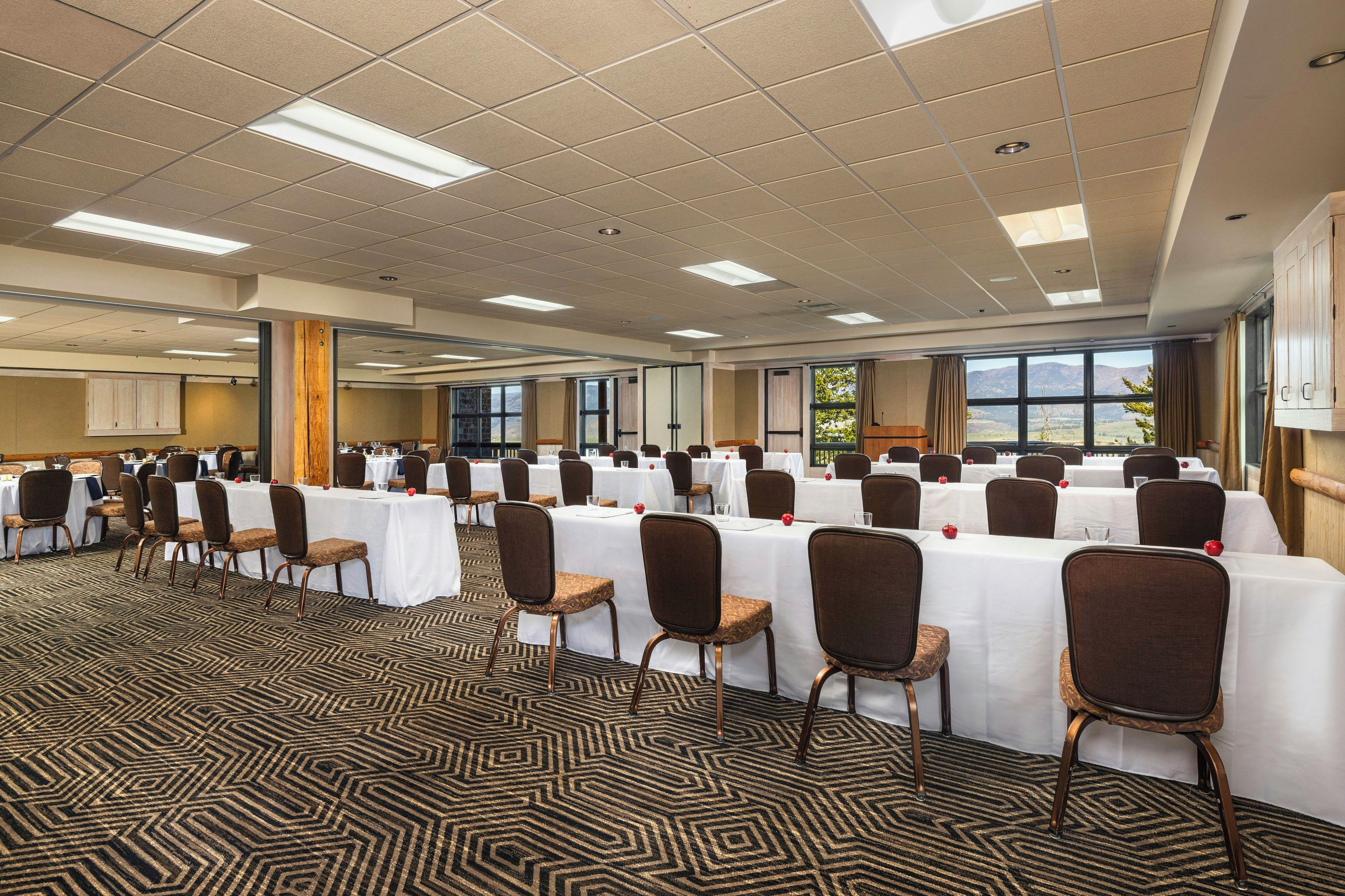 A conference room with multiple tables and chairs, large windows, and a patterned carpet.
