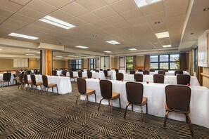 Une salle de conférence dotée de plusieurs tables et de chaises, de grandes fenêtres et d’un tapis à motifs.