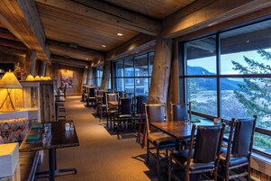 Um restaurante acolhedor com interiores de madeira e grandes janelas que oferecem vista para as montanhas.