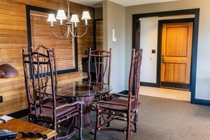 A dining area with a glass table surrounded by wicker chairs, a chandelier, and wooden paneling on the walls.
