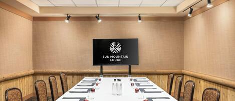 Ett konferensrum med ett långt bord, stolar, en tv-skärm och en logotyp på väggen.