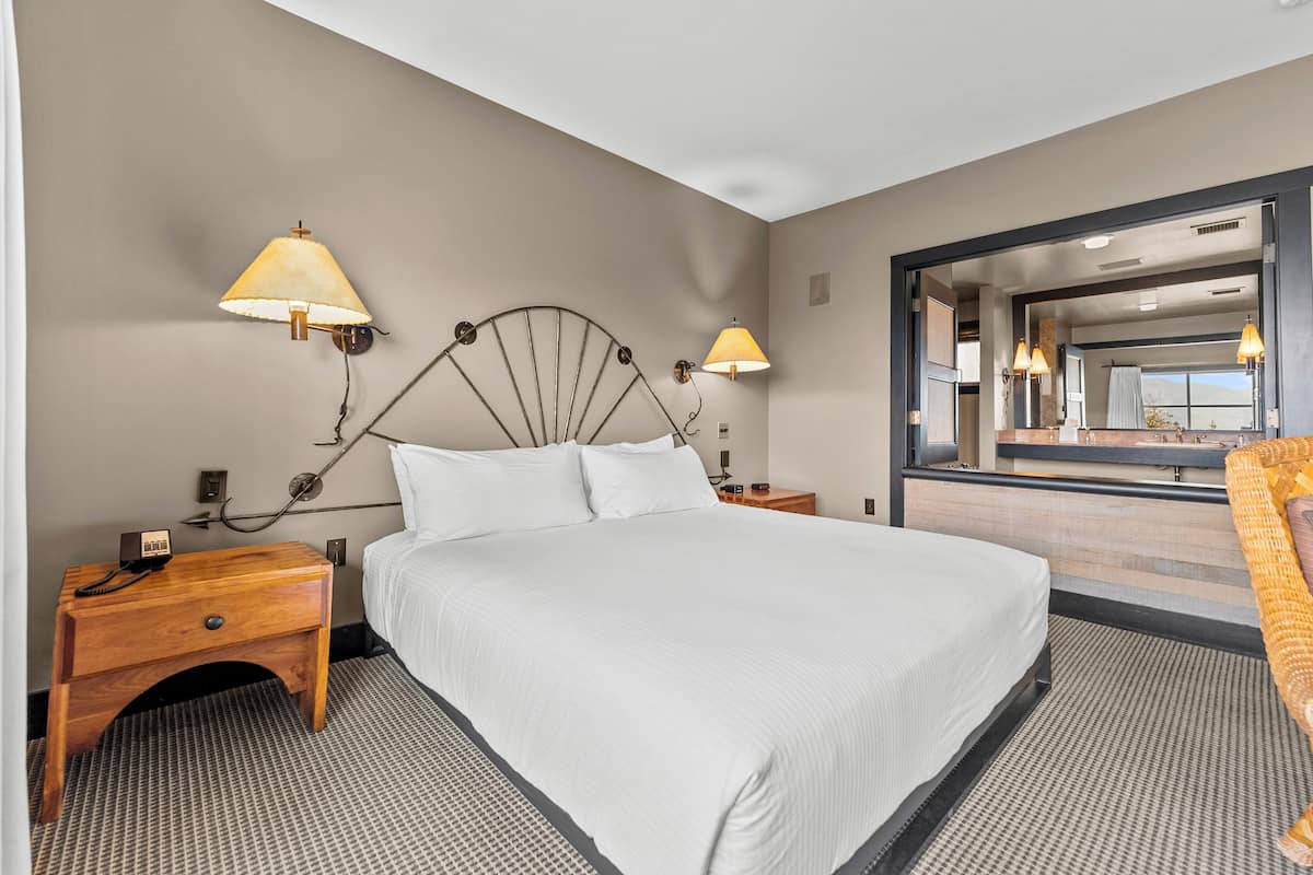 A hotel room with a large bed, two bedside tables, a nightstand, a mirror, and a view of the bathroom.